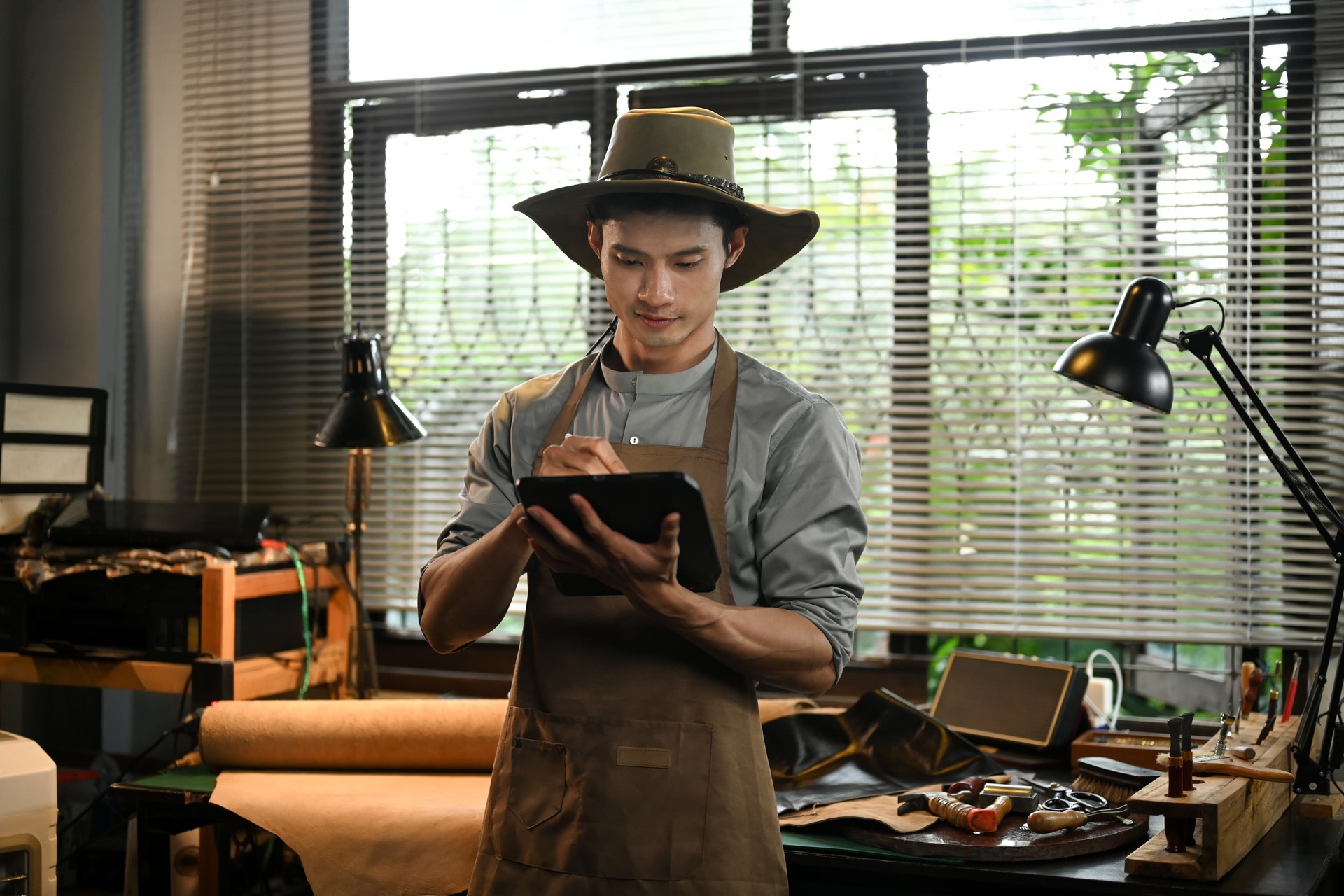 Handsome male leather craftsman taking online orders on digital tablet. Small business and technology concept